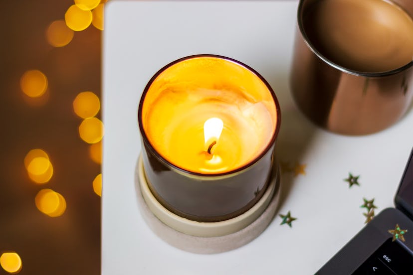 Defocused background with golden candle burns on a white table near a laptop and a cup of coffee. Ar...
