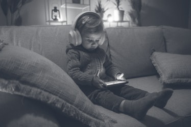 A child on a couch at home, wearing headphones and staring at a tablet.