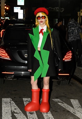 A guest is seen wearing a black and green jacket, white top, red beret and red boots outside the Col...
