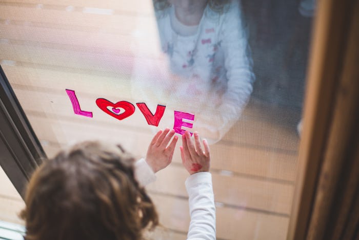 Little girl puts up the letters LOVE on a window for Valentines day, focus on hands holding an E.