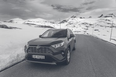 Toyota SUV on the road in front of snowcapped mountain ranges near Krossbu, Jotunheimen National Par...