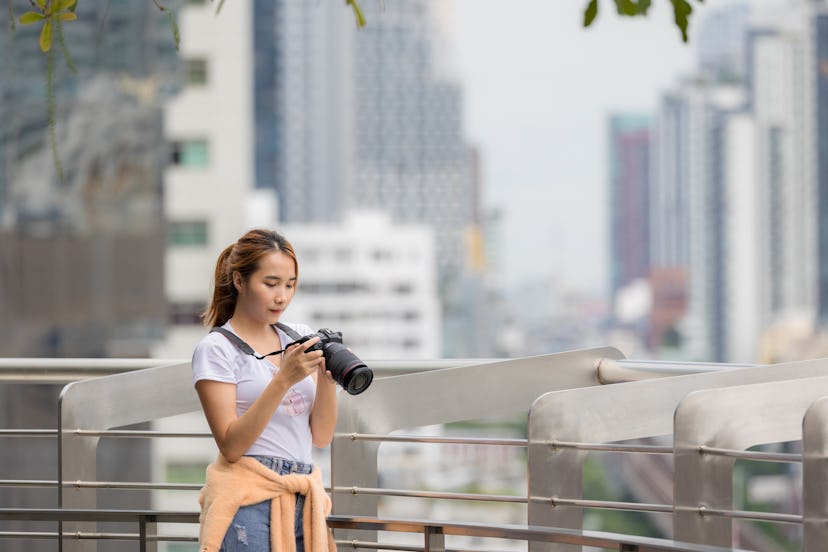 Asian woman using camera for taking a photo in the city while traveling abroad.