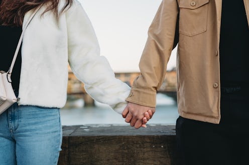 Close up shot of a couple holding hands in Florence with Ponte Vecchio bridge in the background. Lov...
