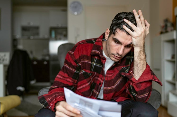 Man checking bills at home, looking frustrated.