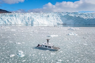 aerial view of a tourist boat with a man on the top with open hands in the middle of the ice in fron...