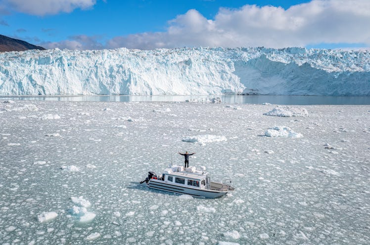aerial view of a tourist boat with a man on the top with open hands in the middle of the ice in fron...