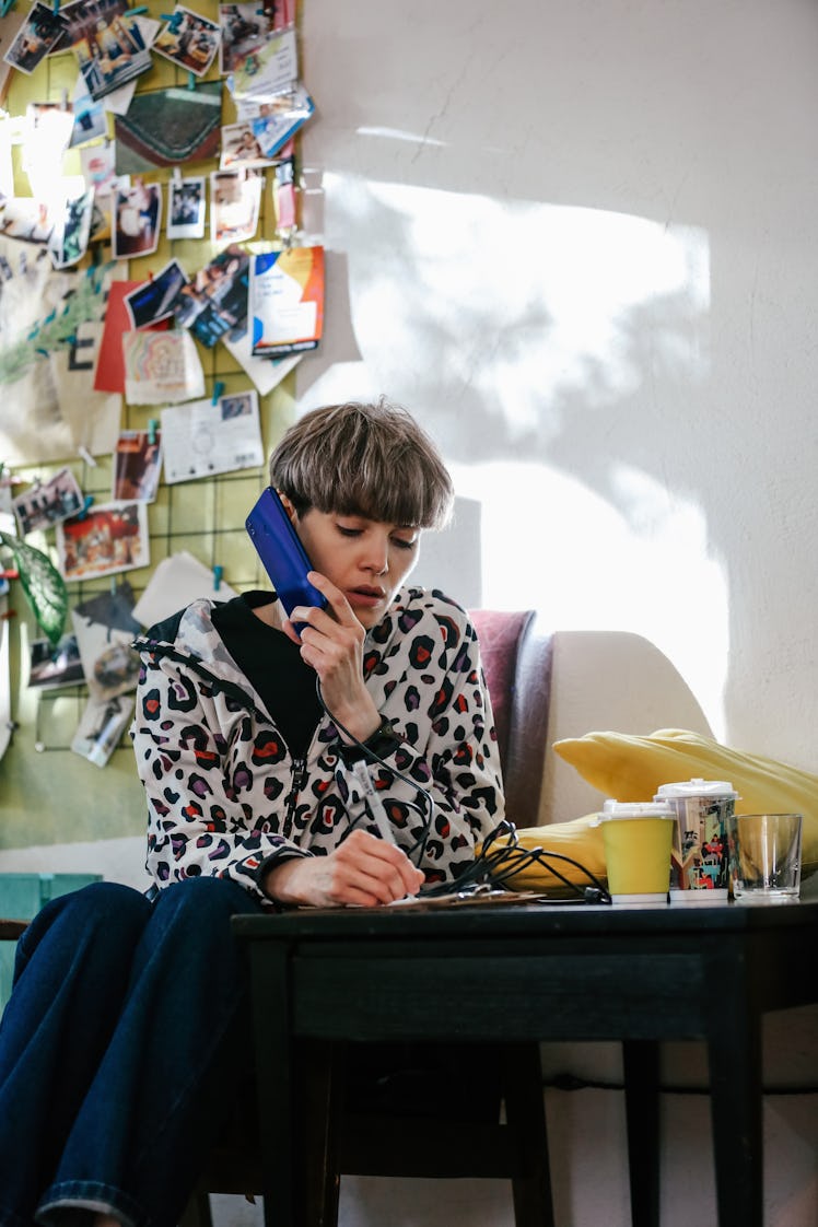 a young woman talks on the phone and writes information down as she considers how her zodiac sign wi...