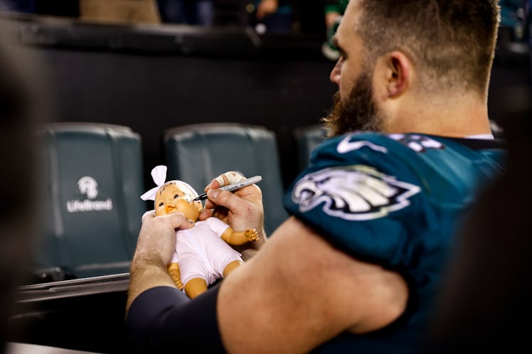 Jason Kelce #62 of the Philadelphia Eagles signs a baby doll for a fan after an NFL divisional round...