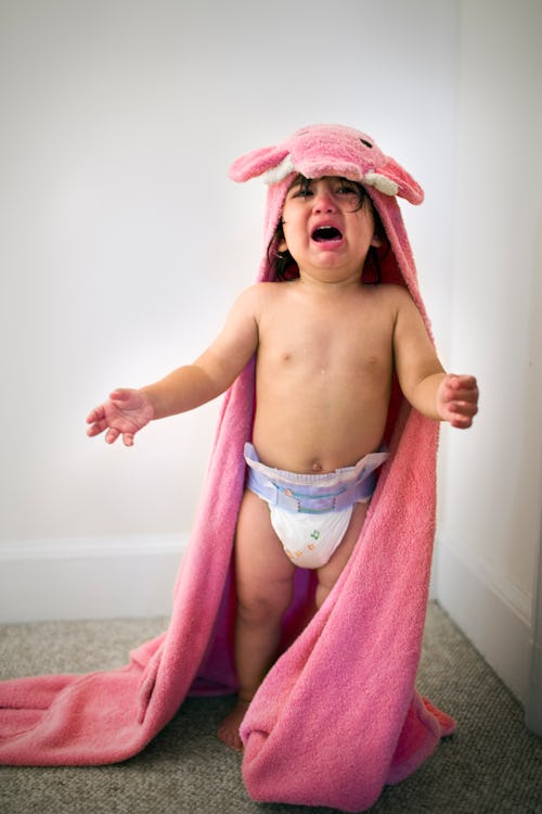 Toddler in pink towel crying after bath time, in a story about how to soothe your baby based on thei...