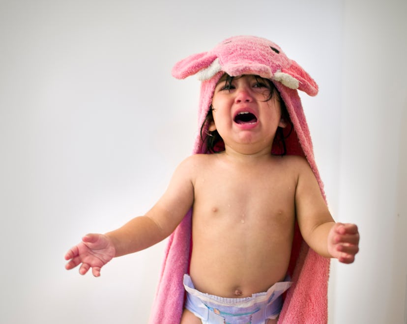 Toddler in pink towel crying after bath time, in a story about how to soothe your baby based on thei...