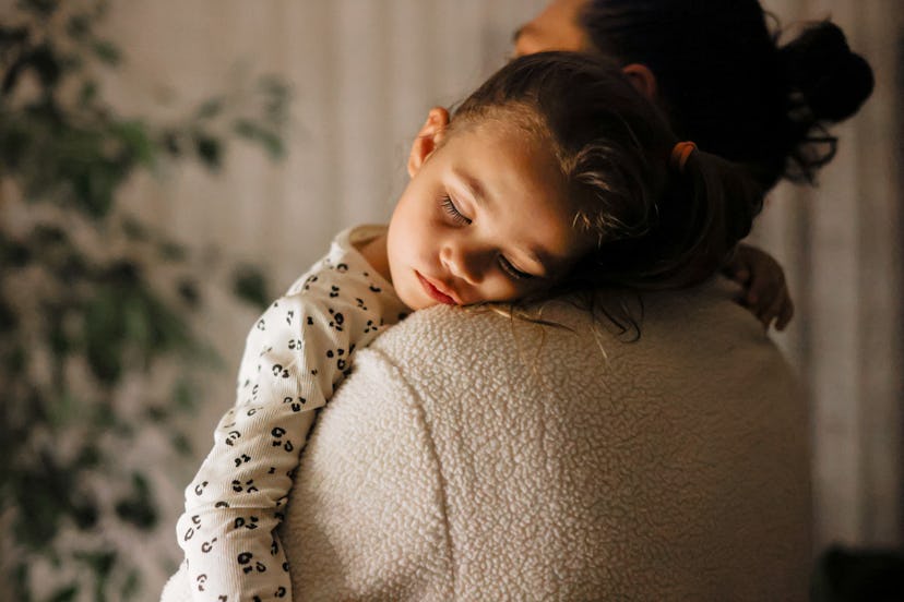 Young girl a sleep on in her moms arms, in an article about the 18 month sleep regression.