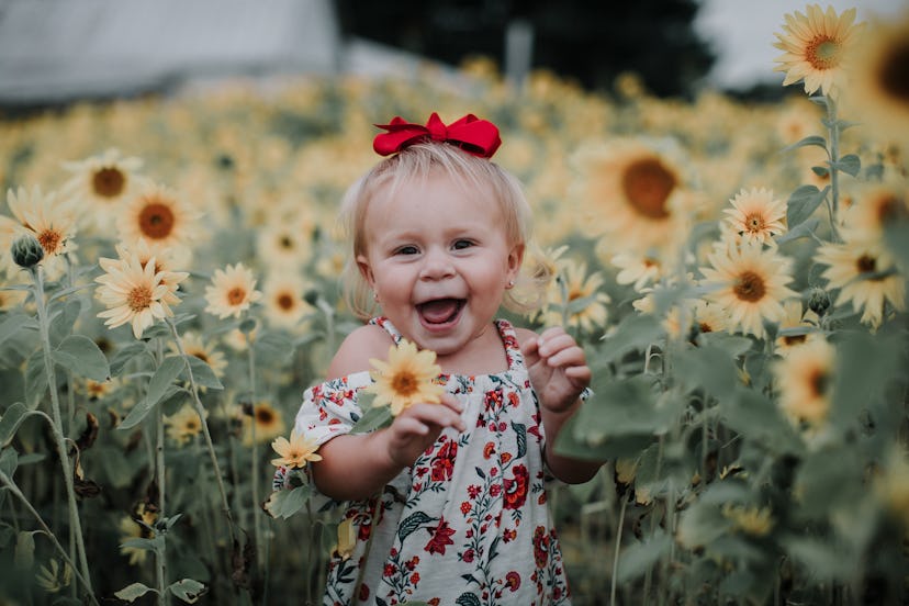 Baby girl smiles in a sunflower field, in a story about baby names that mean red.