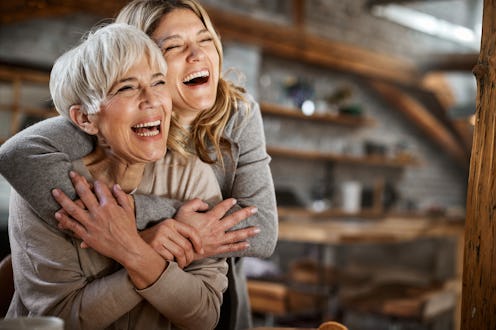 Embraced adult daughter and her mature single mother having fun while laughing at home.