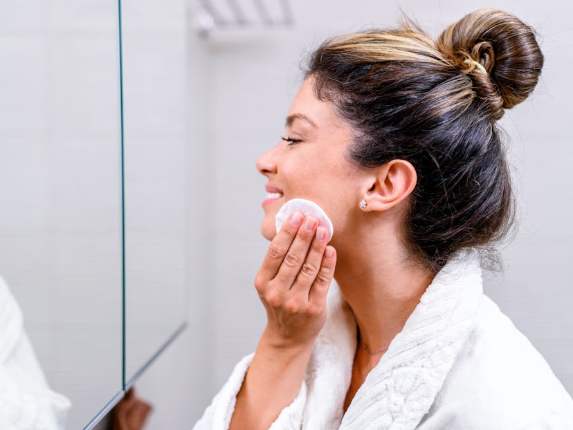 Portrait of a beautiful woman in a bathrobe looking herself in the mirror and cleaning her face.