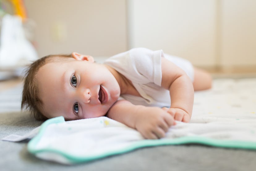 A playful baby looks happy while laying on their side, in a story about baby names that mean red.