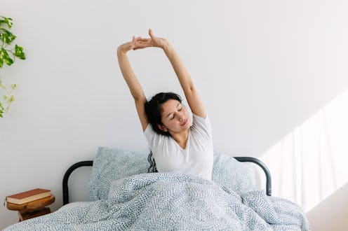 Young teenage Latin American girl stretching on bed in the morning after wake up