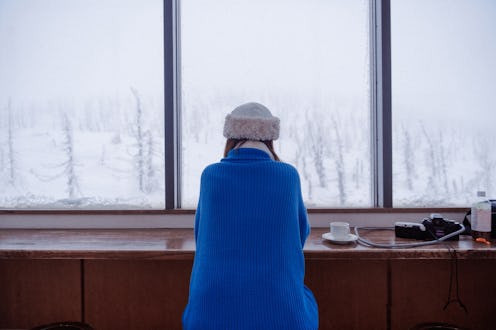 Half-length back view of young Asian adult woman, wearing warm winter clothing, sitting and looking ...