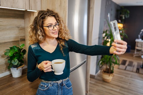 Young woman drinking coffee and taking selfies on her phone
