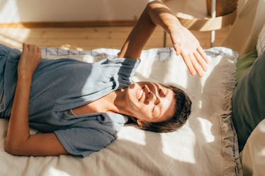 young woman blocks sunlight from her face and smiles as she considers how her zodiac sign affects he...