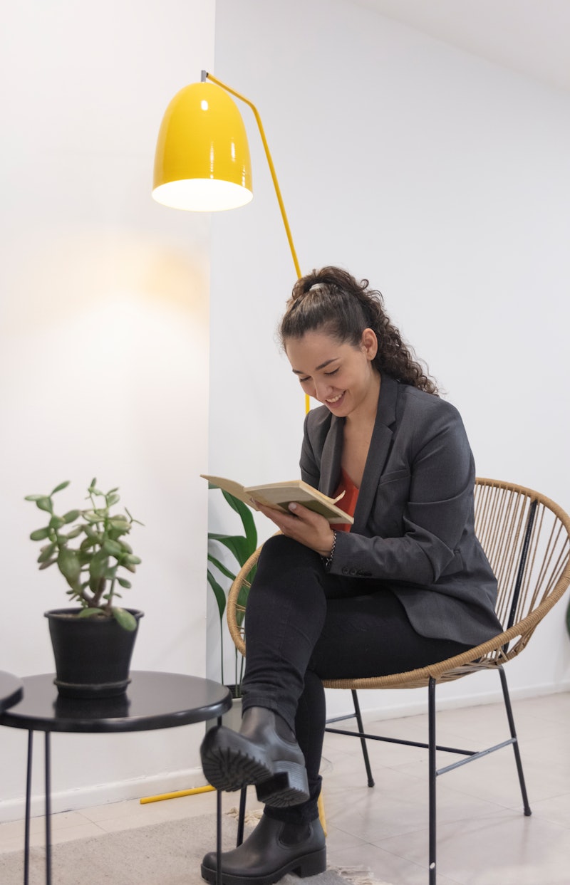 A happy businesswoman is reading a book at her workplace