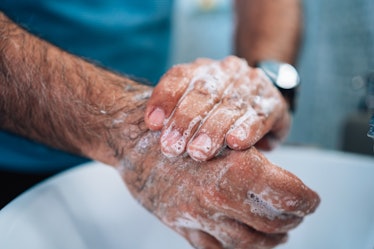 Close up mature man standing above the sink and washing hands with soap