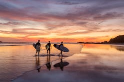 Surfers at sunset walking on beach, Playa Guiones, Nosara, Guanacaste, Costa Rica