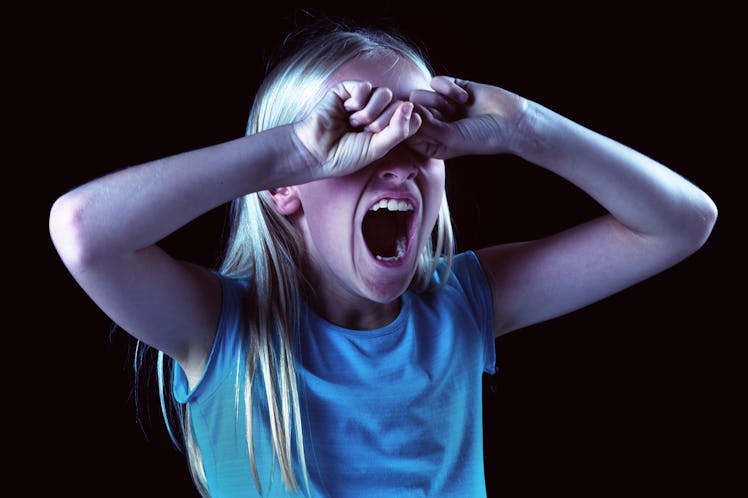 A little blonde girl is seen against a black background, her hands covering her eyes and her mouth w...