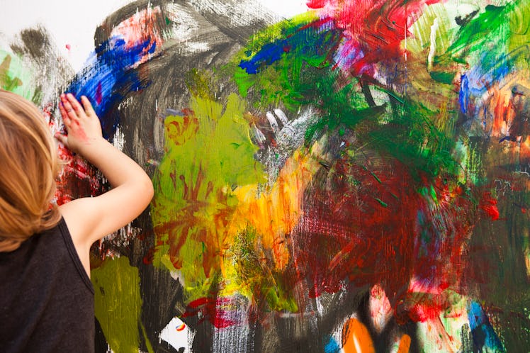 A kid painting on a white wall in different colors with their hands