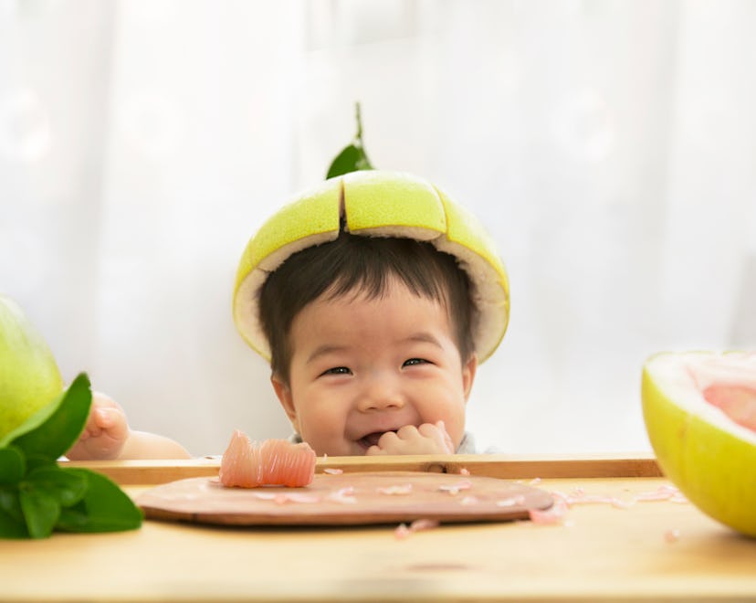 Toddler eating fruits with a pomelo hat, in a story about fruit baby names.