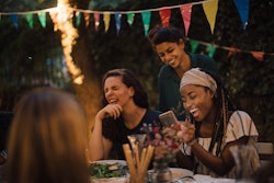 Group of friends laughing at outdoor table while playing party game apps
