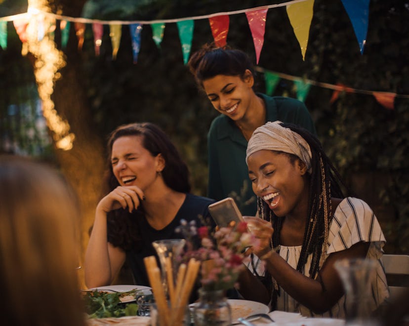 Group of friends laughing at outdoor table while playing party game apps