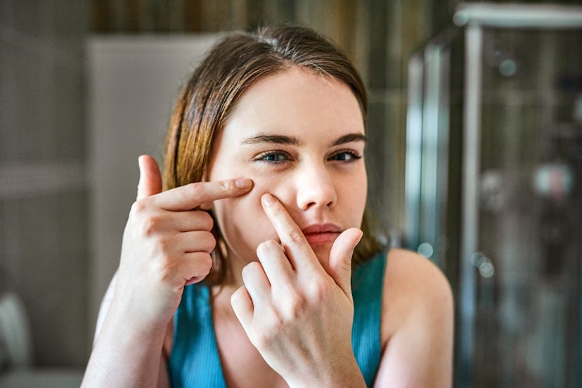 Shot of a young woman squeezing pimples on her face in the bathroom at home