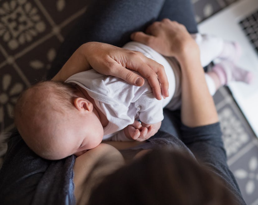 Mom holding baby while researching postpartum psychosis on laptop in bed.
