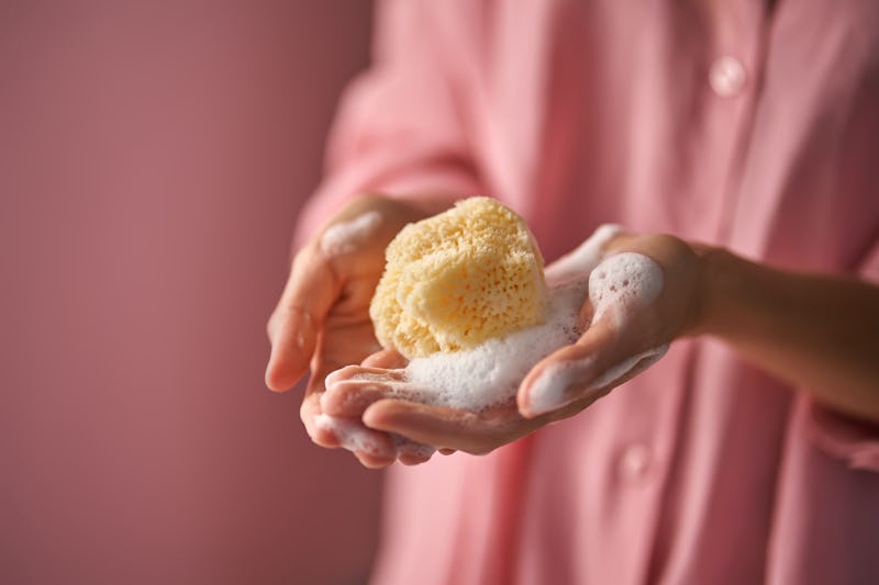 A girl in pink holds in her hand a natural sea sponge for washing a gel for washing in foam.