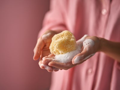 A girl in pink holds in her hand a natural sea sponge for washing a gel for washing in foam.