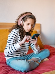  teenage girl sitting cross-legged on her bed using a smart phone. TikTok implemented an update to t...