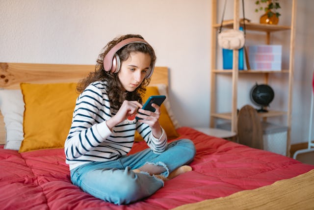 teenage girl sitting cross-legged on her bed using a smart phone. TikTok implemented an update to t...