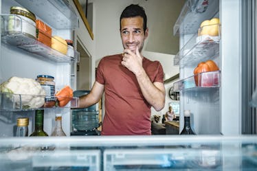 Worried man thinking what to choose from his fridge in the kitchen.