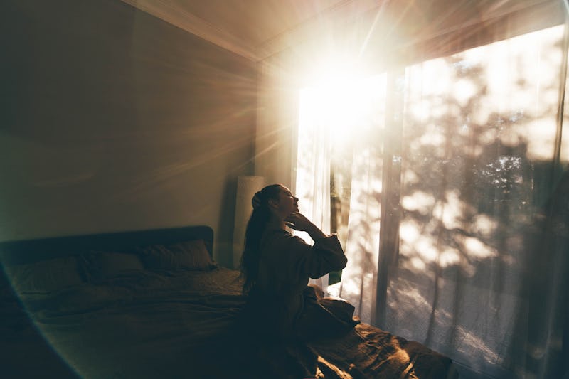 Young woman in bathrobe who has just woken up enjoys the rays of the morning sun.