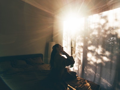 Young woman in bathrobe who has just woken up enjoys the rays of the morning sun.