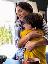 A waist-up shot of a mother hugging her son next to the kitchen counter looking happy with her son. ...