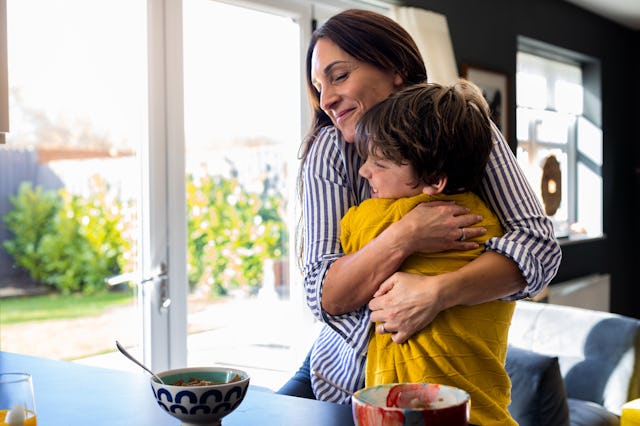 A waist-up shot of a mother hugging her son next to the kitchen counter looking happy with her son. ...