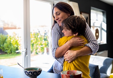 A waist-up shot of a mother hugging her son next to the kitchen counter looking happy with her son. ...