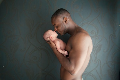 Dark/Black skin father and newborn white baby girl having nose to nose contact. Dark background.