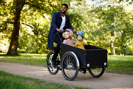 A father pushing his two kids in a cart, surrounded by nature.