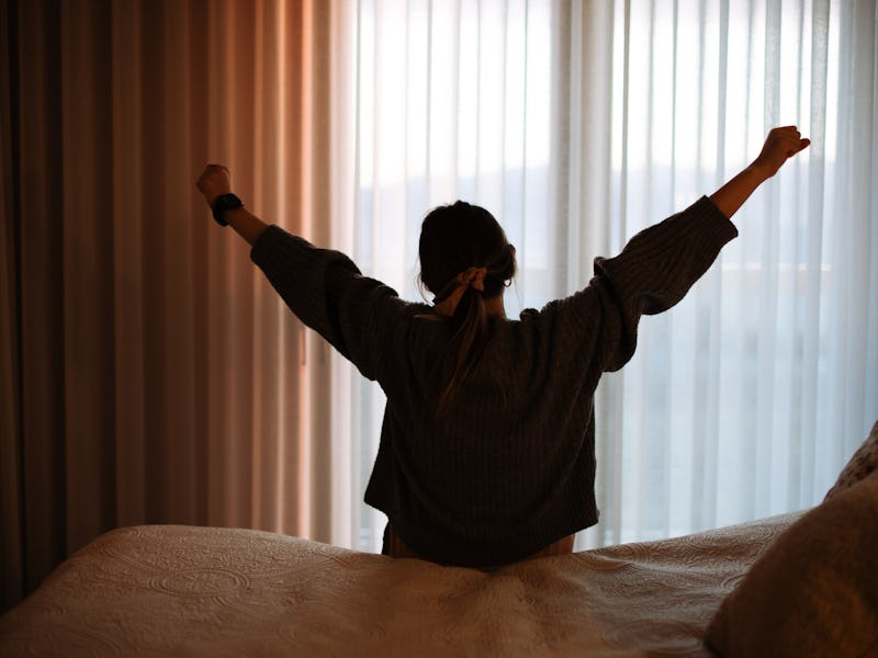 Young woman streching in bed in the morning while looking at the sunrise.