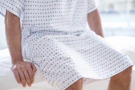 A man wearing hospital gown sitting on bed.