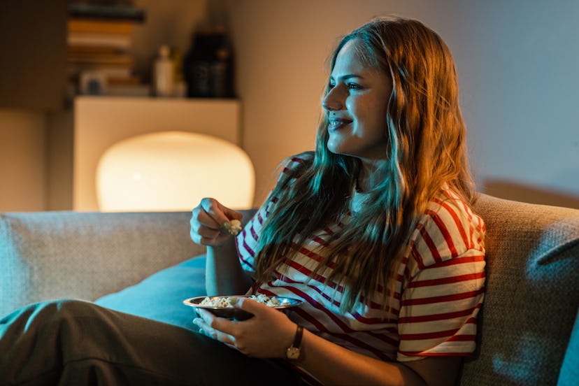 Young woman eating popcorns and watching a show on TV.