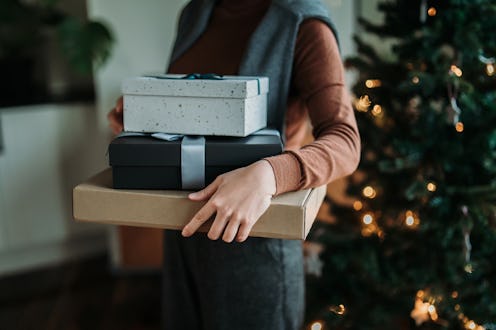 Cropped shot of young Asian woman holding stack of wrapped Christmas presents in hands, standing nex...