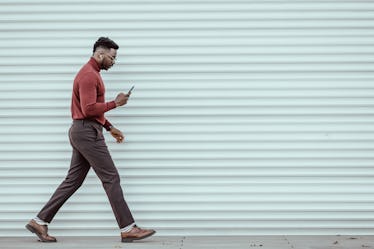 Portrait of African-American young businessman using smartphone while walking